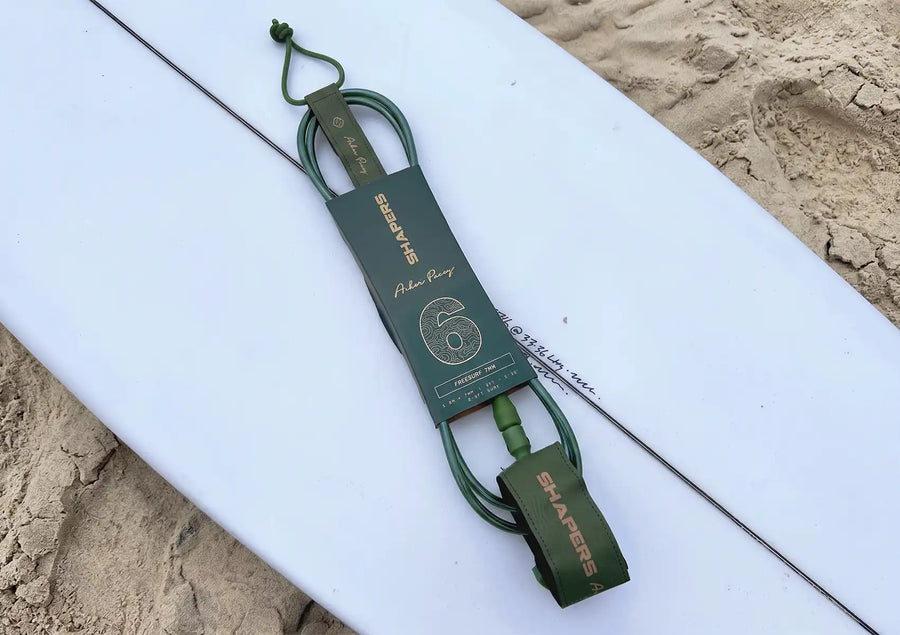 Surf leash coiled by a board tail showing the cuff, rail saver and cord.