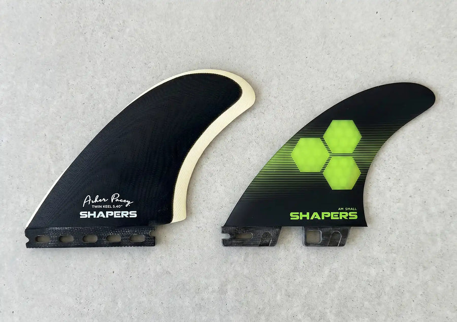 Side-by-side view comparing a black twin keel fin with a full Futures base next to a thruster fin with a dual-tab FCS II base to show futures vs fcs fins.